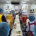 新業(yè)同仁與志工們繫上圍裙、套上防塵帽，戴上口罩，手捧一份份飯包各司其職，為的是準(zhǔn)時(shí)將熱騰騰的飯包送到長(zhǎng)輩手中。