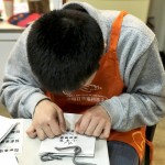 小羊苗朋友將臉湊近提袋上，仔細將貼紙慢慢地貼上，盡可能確保貼紙有貼正不歪斜。從肢體動作，可以曉得小羊們做每件事比別人費力，但不減心意。