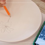 筆尖在素色瓷胚上，輕輕滑過，對照著手機(jī)上的圖樣，描繪形塑出個(gè)人獨(dú)特的風(fēng)格。