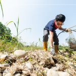 從石縫中抽出韌性的橡膠圈，岸邊的垃圾也不可輕忽，可能會因為漲潮後的潮水而沖刷到溪裡。